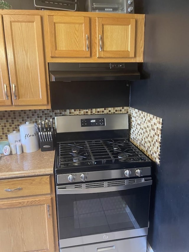 kitchen featuring under cabinet range hood, tasteful backsplash, stainless steel range with gas cooktop, and light countertops