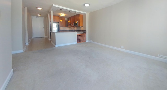 kitchen with stainless steel appliances, dark stone counters, brown cabinetry, baseboards, and light colored carpet