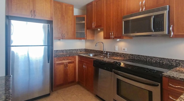 kitchen featuring brown cabinetry, dark stone countertops, appliances with stainless steel finishes, and a sink