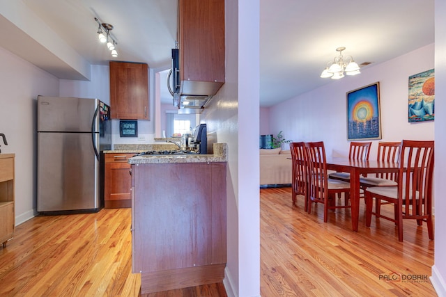 kitchen featuring track lighting, light wood-type flooring, brown cabinets, freestanding refrigerator, and an inviting chandelier