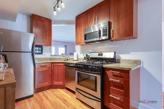 kitchen featuring light wood-type flooring, stainless steel appliances, light stone counters, and brown cabinetry