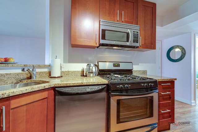 kitchen with light wood finished floors, baseboards, light stone countertops, stainless steel appliances, and a sink