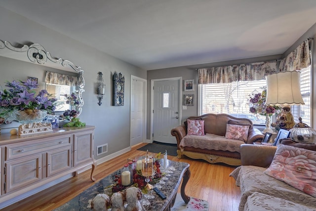 living room featuring light wood finished floors, visible vents, plenty of natural light, and baseboards