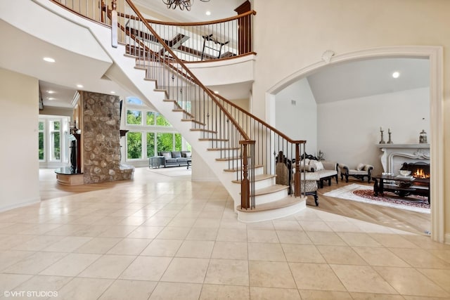 entrance foyer featuring light tile patterned floors, a high ceiling, a warm lit fireplace, and stairs