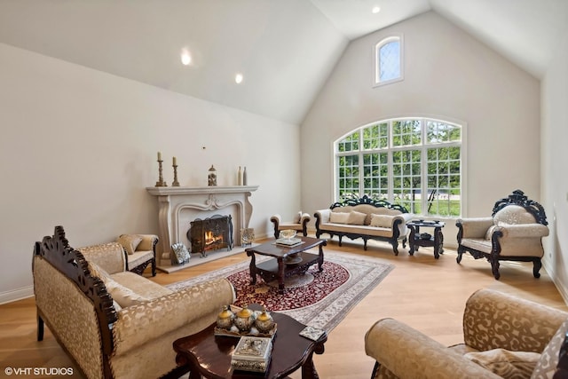 living area with baseboards, high vaulted ceiling, a warm lit fireplace, and wood finished floors