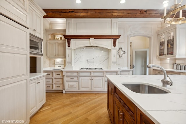 kitchen with light wood-type flooring, a sink, light stone counters, backsplash, and stainless steel appliances