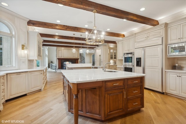 kitchen featuring a large island, built in appliances, light wood-type flooring, and a sink