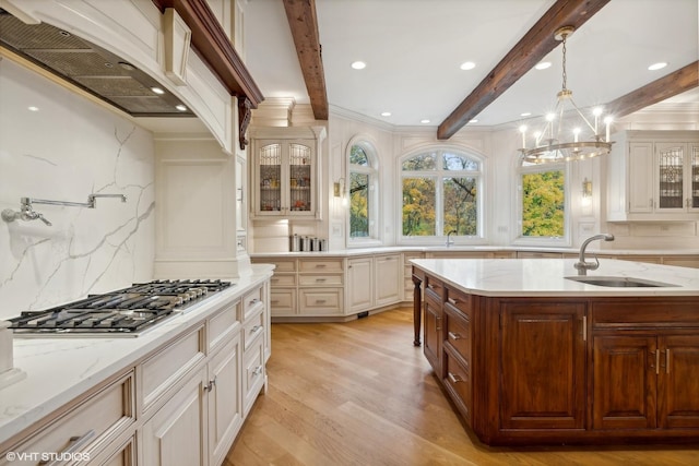 kitchen featuring beamed ceiling, a sink, stainless steel gas stovetop, glass insert cabinets, and custom exhaust hood