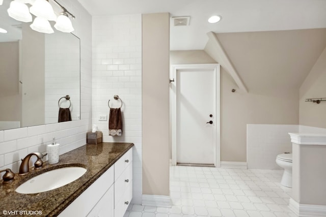 bathroom featuring vanity, baseboards, visible vents, tile walls, and toilet