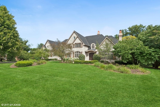 french provincial home with stone siding, a chimney, and a front lawn