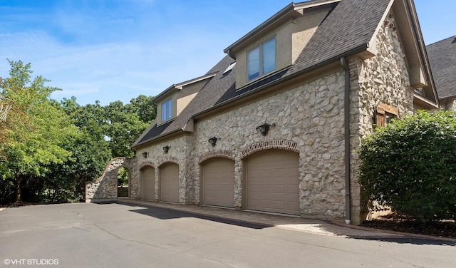 view of home's exterior with a garage, stone siding, a shingled roof, and stucco siding