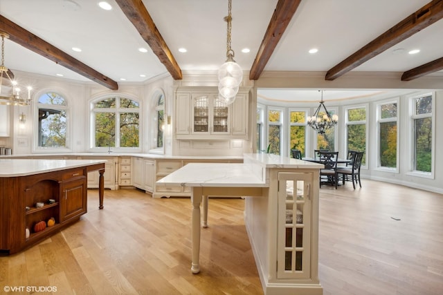 kitchen featuring a notable chandelier, pendant lighting, a kitchen island, light wood finished floors, and glass insert cabinets