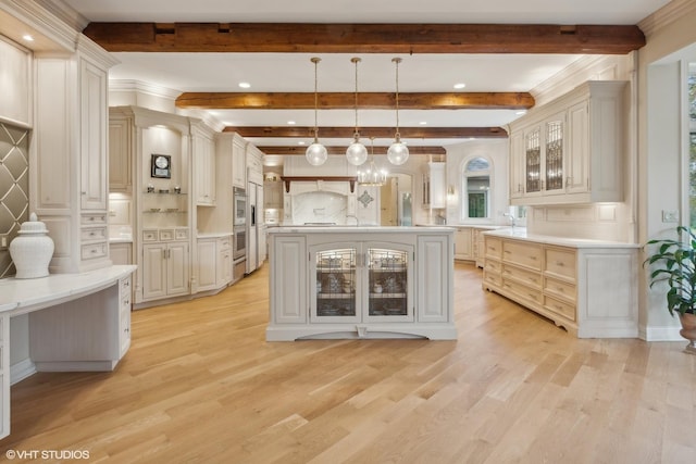 kitchen with a kitchen island with sink, light wood-style floors, double oven, glass insert cabinets, and hanging light fixtures