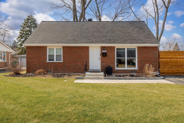 view of front facade featuring brick siding, roof with shingles, a front lawn, and fence