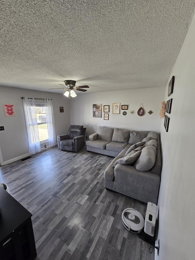 living room with a ceiling fan, dark wood-style floors, visible vents, and a textured ceiling