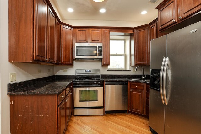 kitchen with light wood-type flooring, dark stone countertops, recessed lighting, stainless steel appliances, and a sink