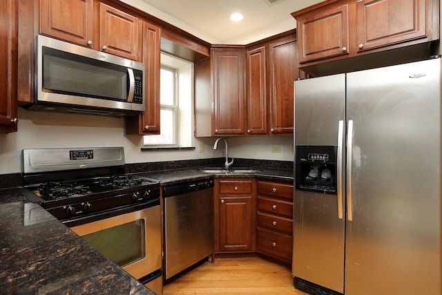 kitchen with a sink, stainless steel appliances, light wood-style floors, and dark stone countertops