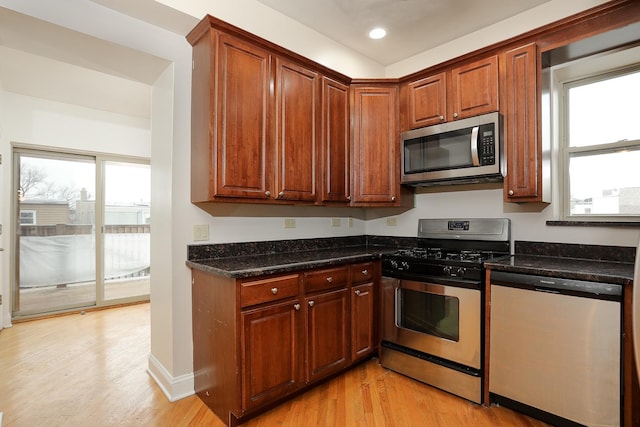 kitchen featuring stainless steel appliances, dark stone counters, and light wood finished floors