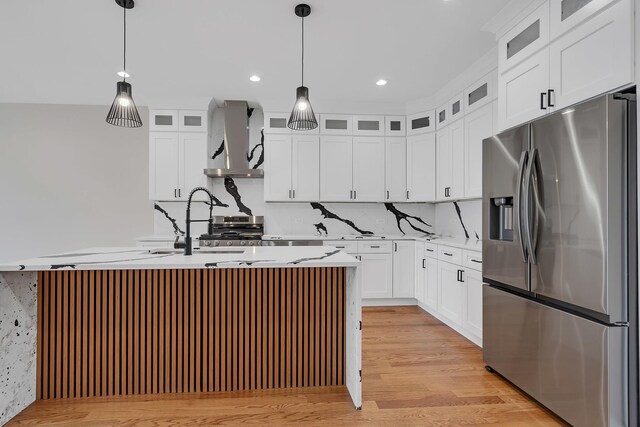 kitchen featuring wall chimney range hood, open floor plan, light countertops, stainless steel appliances, and a kitchen island with sink