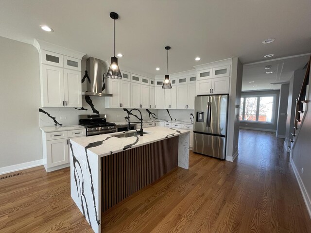 kitchen featuring white cabinets, appliances with stainless steel finishes, wall chimney range hood, and a sink