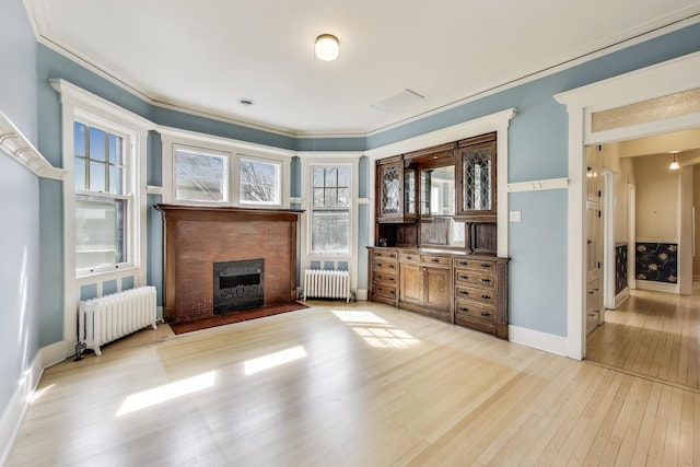 unfurnished living room featuring radiator heating unit, light wood-type flooring, a fireplace with flush hearth, and ornamental molding