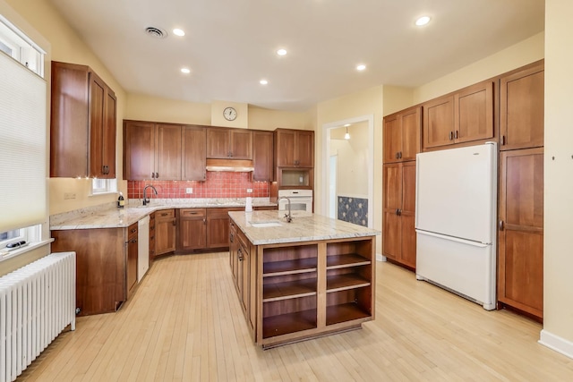 kitchen featuring light wood finished floors, radiator, under cabinet range hood, white appliances, and open shelves