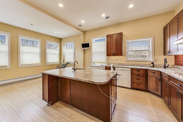 kitchen featuring visible vents, light wood-style flooring, an island with sink, a sink, and dishwasher