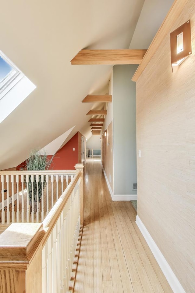 hallway featuring baseboards, vaulted ceiling with skylight, and hardwood / wood-style floors