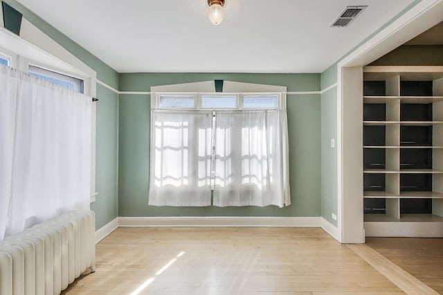 empty room featuring radiator, wood finished floors, visible vents, and baseboards