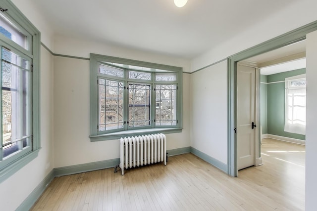 empty room featuring radiator heating unit, baseboards, and wood-type flooring