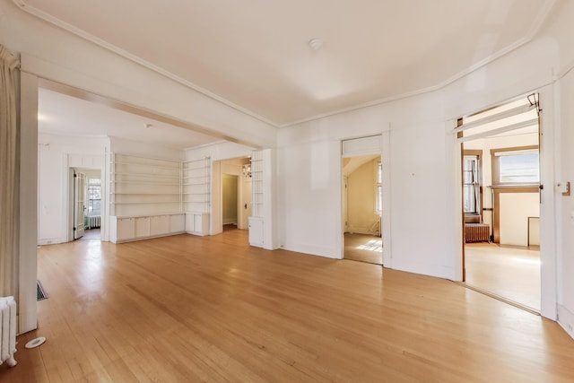 interior space featuring crown molding, radiator heating unit, light wood-style floors, and a healthy amount of sunlight