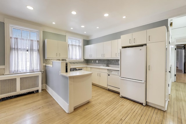 kitchen with white appliances, light wood finished floors, a peninsula, radiator heating unit, and light countertops