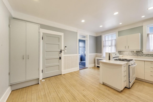 kitchen with a peninsula, gas range gas stove, light countertops, wainscoting, and light wood-type flooring