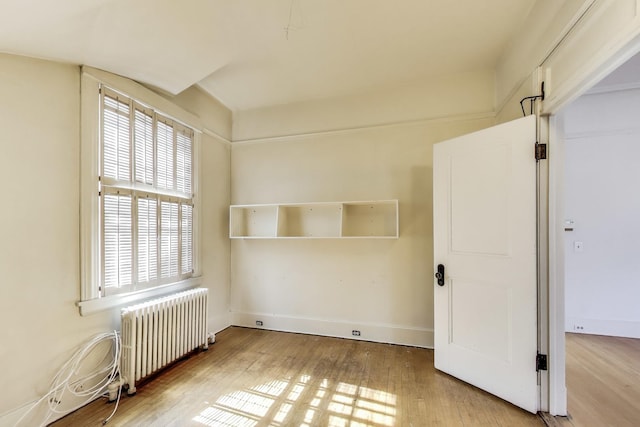 unfurnished room with baseboards, radiator, and wood finished floors