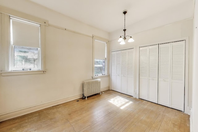 unfurnished bedroom with radiator, light wood-style floors, multiple closets, and a chandelier