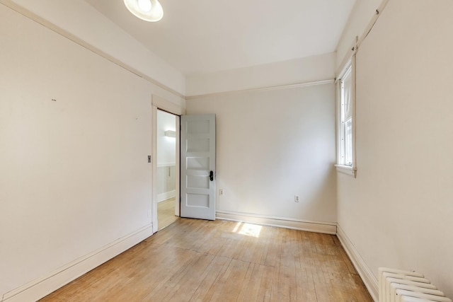 empty room with baseboards, radiator, and light wood finished floors