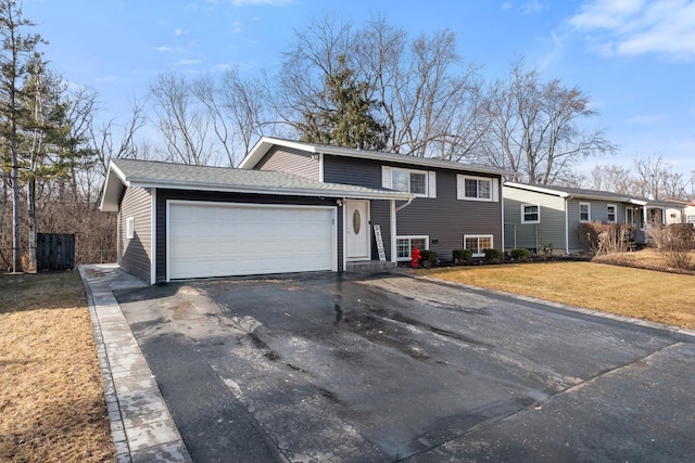 split level home with aphalt driveway, an attached garage, roof with shingles, and a front yard