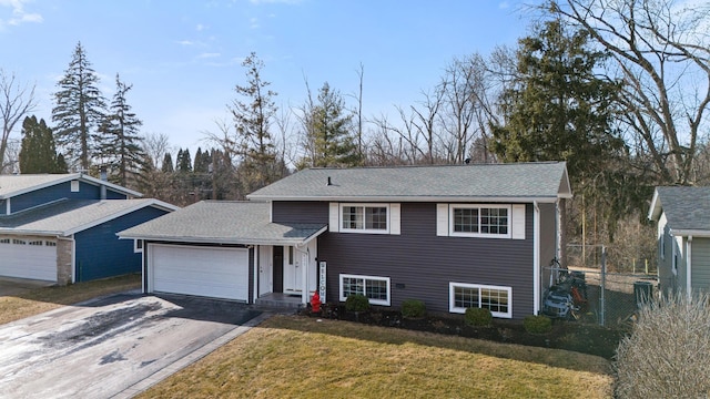 split level home with a front yard, fence, driveway, roof with shingles, and an attached garage