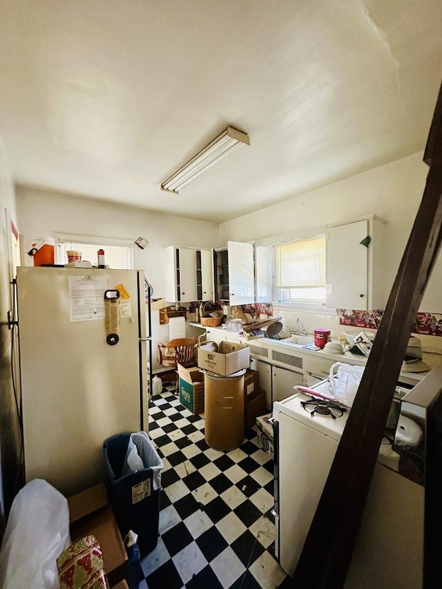 kitchen featuring light floors, light countertops, freestanding refrigerator, white cabinetry, and a sink