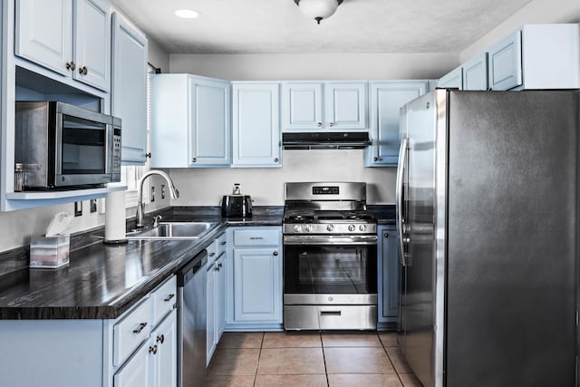 kitchen with dark countertops, under cabinet range hood, appliances with stainless steel finishes, light tile patterned flooring, and a sink