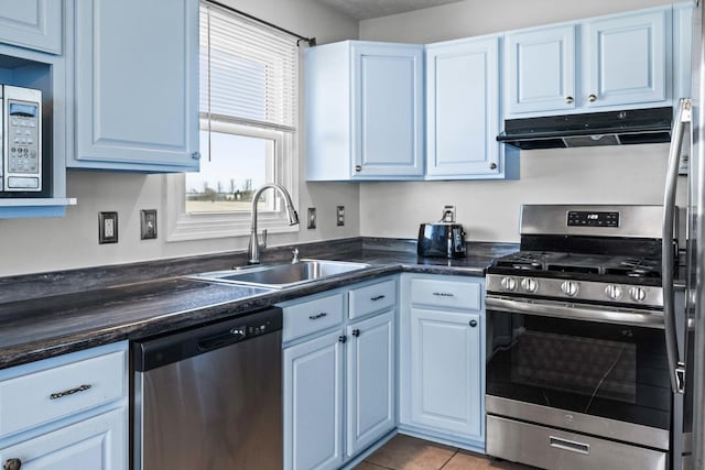 kitchen featuring under cabinet range hood, a sink, dark countertops, appliances with stainless steel finishes, and light tile patterned floors