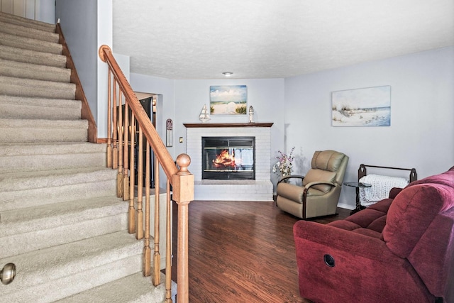 living area with a textured ceiling, wood finished floors, stairway, a fireplace, and baseboards