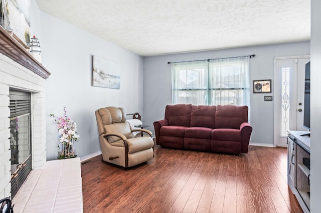 living room featuring a brick fireplace, visible vents, dark wood-style flooring, and a textured ceiling