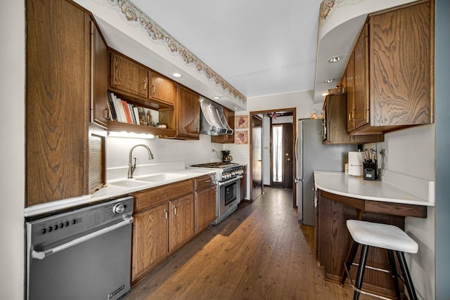 kitchen with dark wood-type flooring, light countertops, stainless steel appliances, wall chimney exhaust hood, and a sink