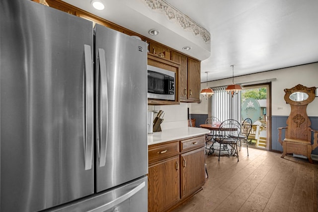 kitchen featuring brown cabinetry, a wainscoted wall, stainless steel appliances, light countertops, and wood-type flooring