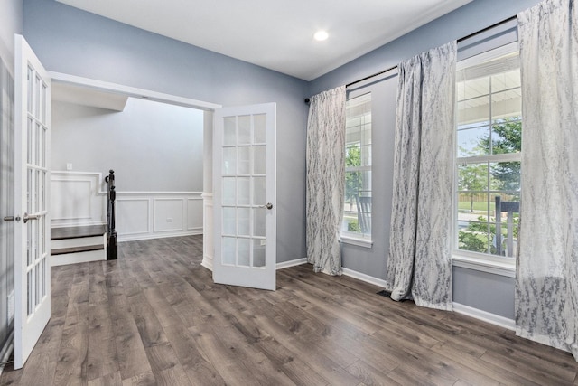 unfurnished room with french doors, wood finished floors, wainscoting, and a decorative wall