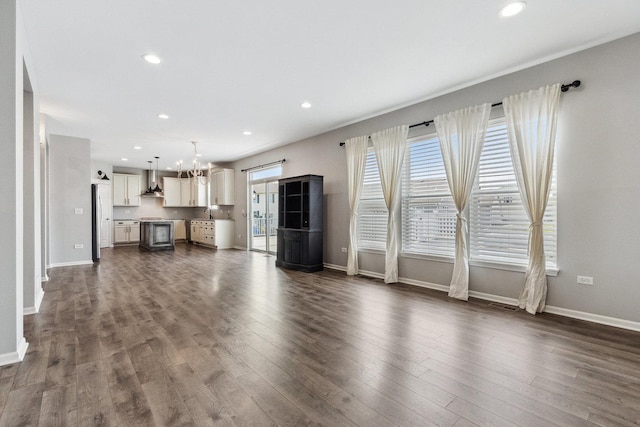 unfurnished living room with an inviting chandelier, dark wood-type flooring, and baseboards