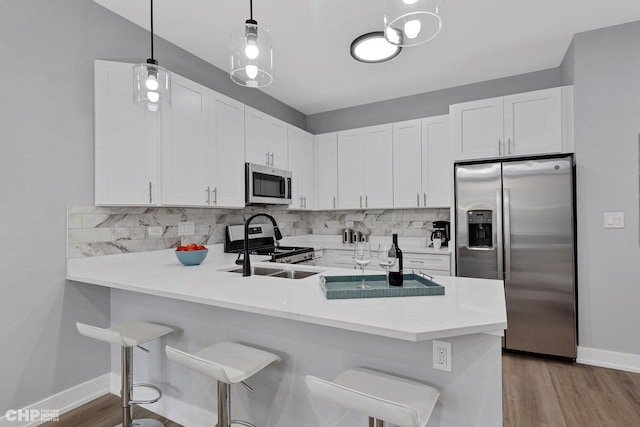 kitchen with a peninsula, stainless steel appliances, decorative backsplash, light countertops, and white cabinets