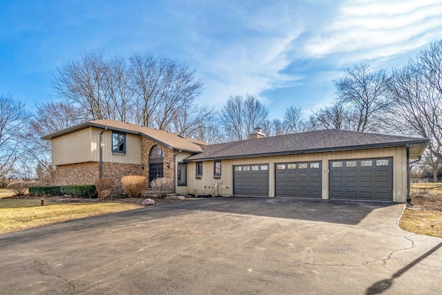 split level home with driveway, an attached garage, roof with shingles, and a chimney