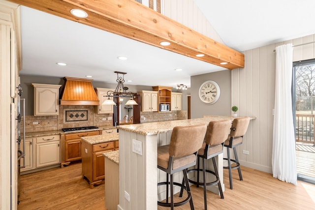 kitchen featuring custom range hood, open shelves, stainless steel microwave, a kitchen island, and light wood-style floors